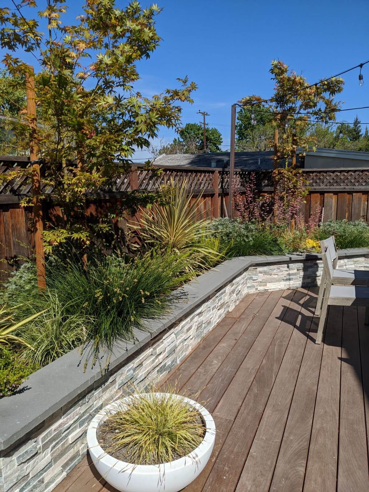 Stone knee wall surrounding wooden deck with natural grasses and plantings