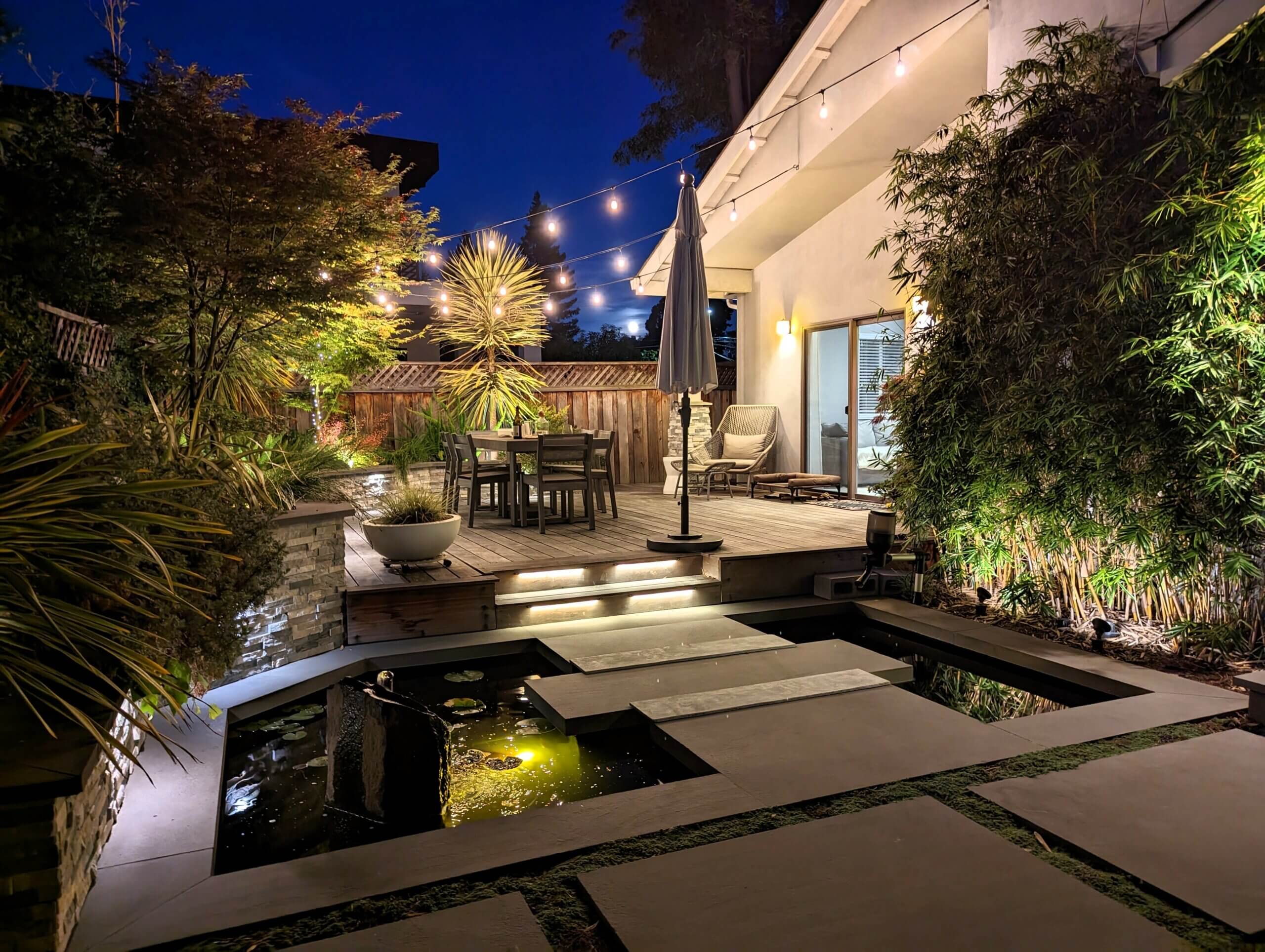 View of backyard zen landscape at night with grown bamboo alongside koi pond