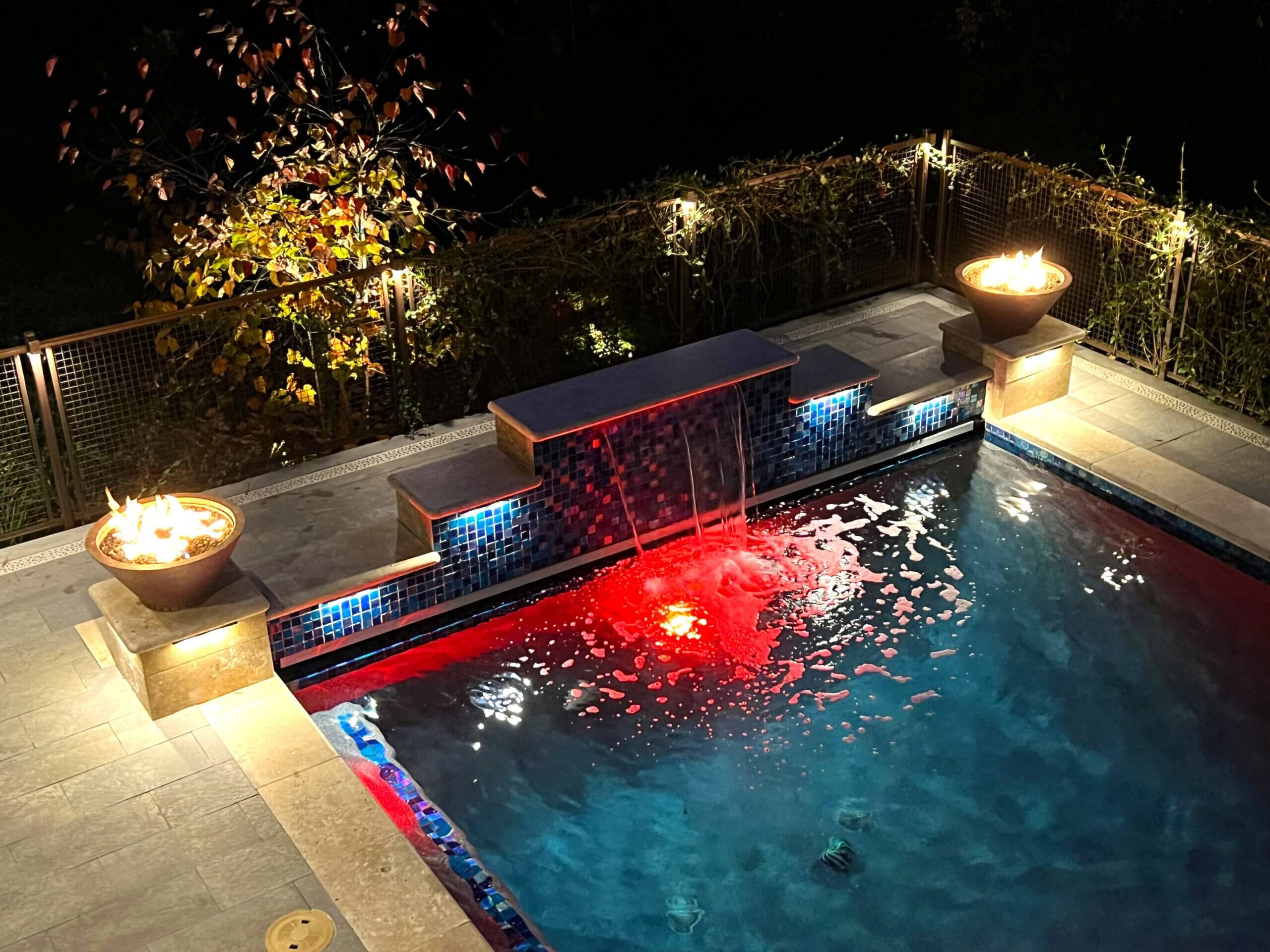 Swimming pool at night with red lights under waterfall feature in Santa Cruz hillside backyard