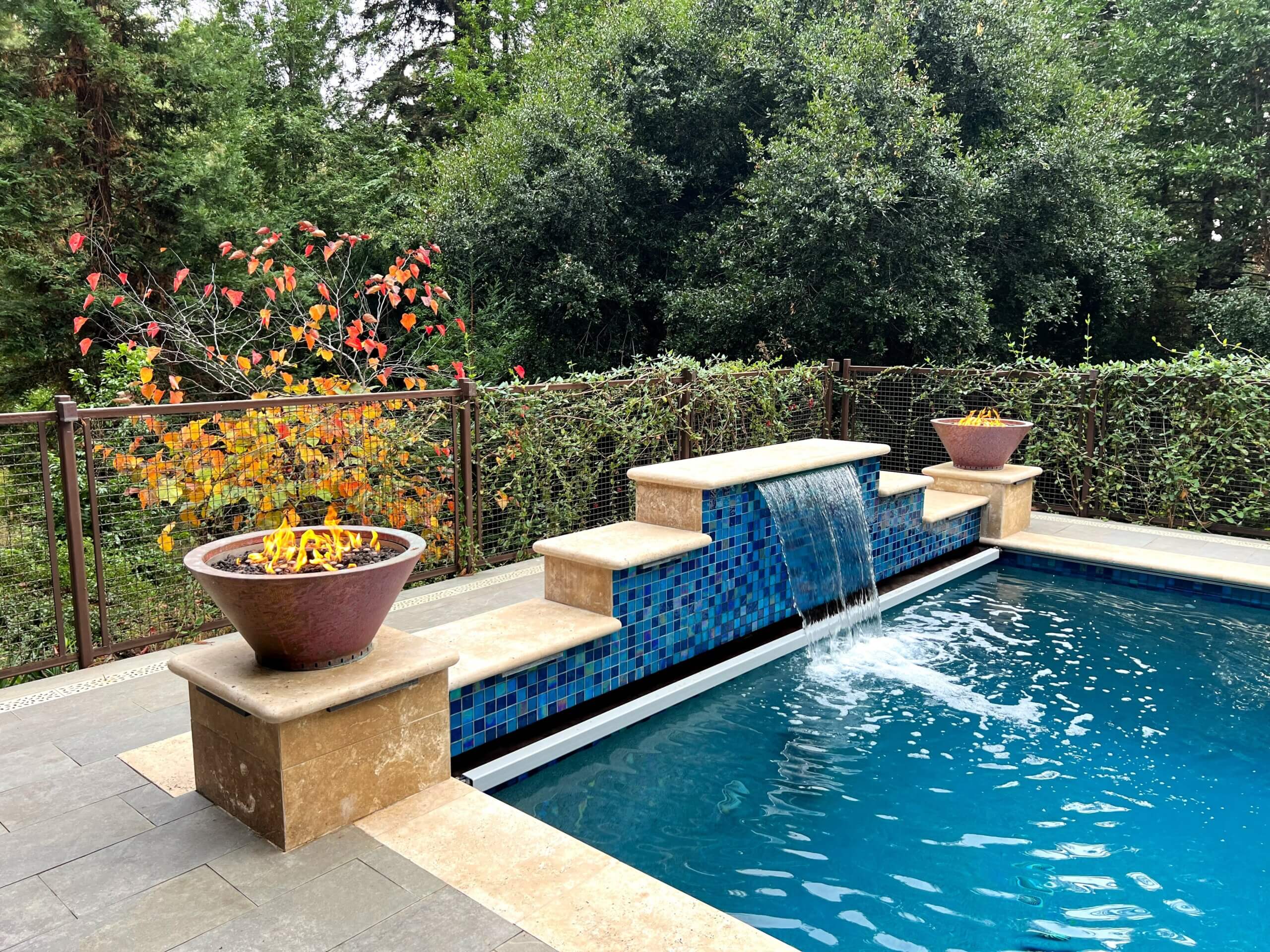 Swimming pool waterfall feature flanked by lit firepits