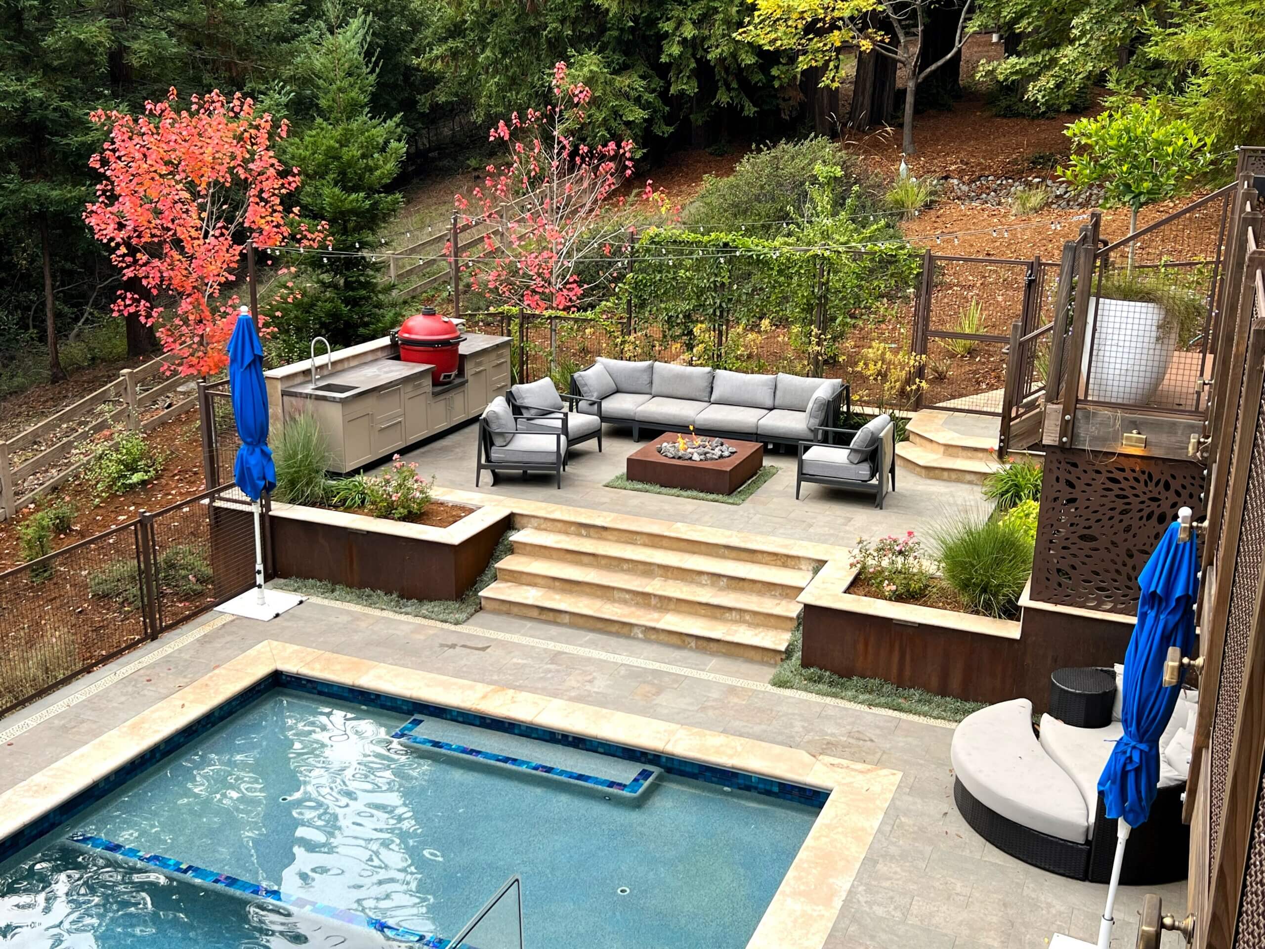 View of raised seating area with firepit and outdoor kitchen in steep sloped backyard in Santa Cruz
