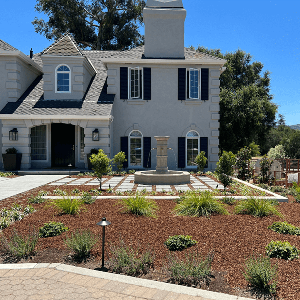 New landscaping and fountain in front of light grey French provincial home