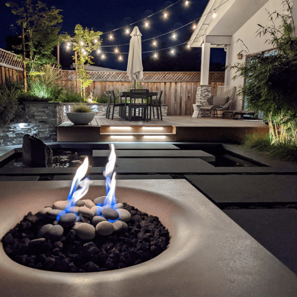 Firepit at night in a zen backyard landscape with large pavers and lighting
