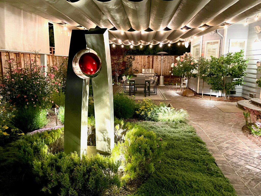 Nightime view of custom landscape with Dale Rogers sculpture as centerpiece beneath a fabric awning