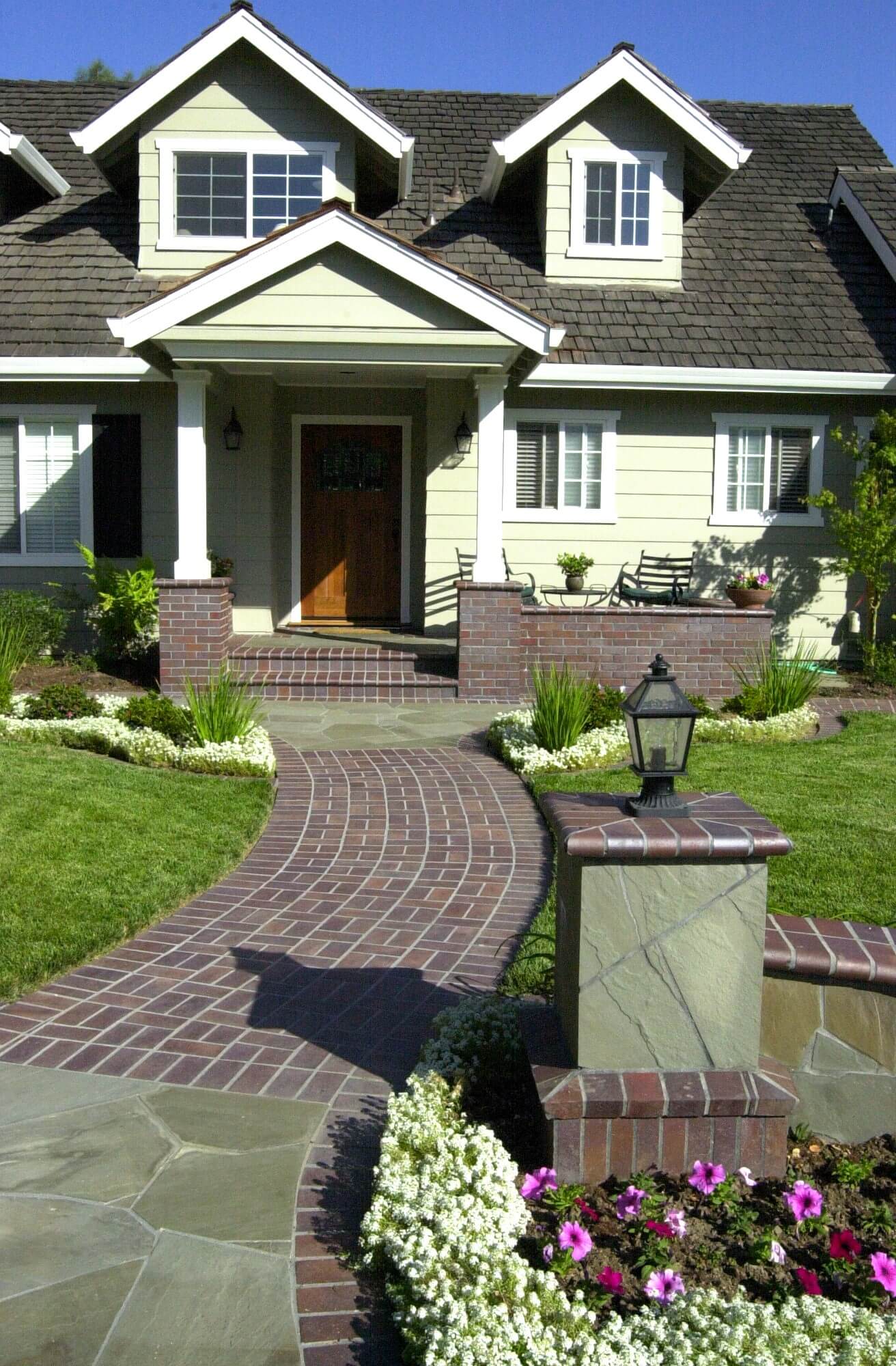Front yard walkway made from a combination of red brick in a unique pattern and irregular paver stone