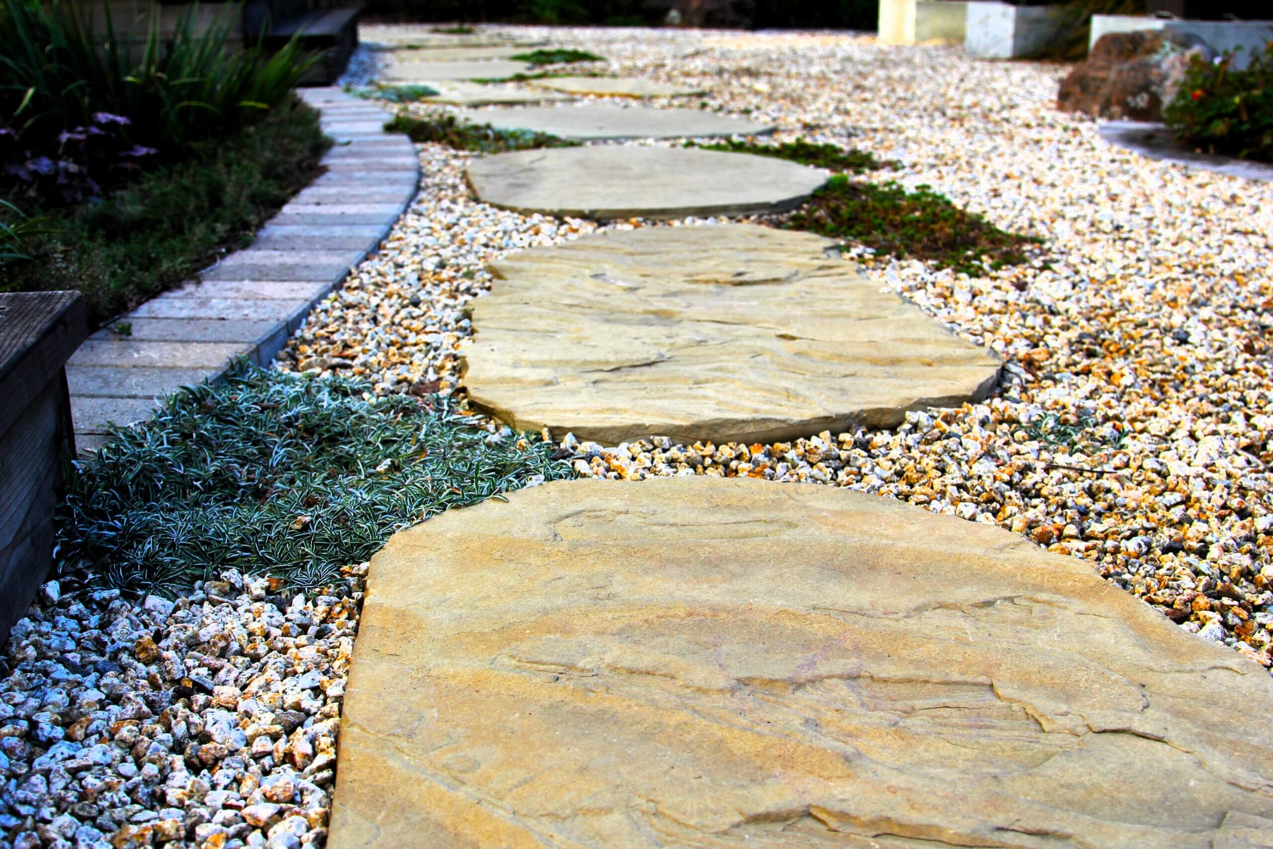 Rough stone pathway surrounded by gravel and bricks with ground cover interspersed.