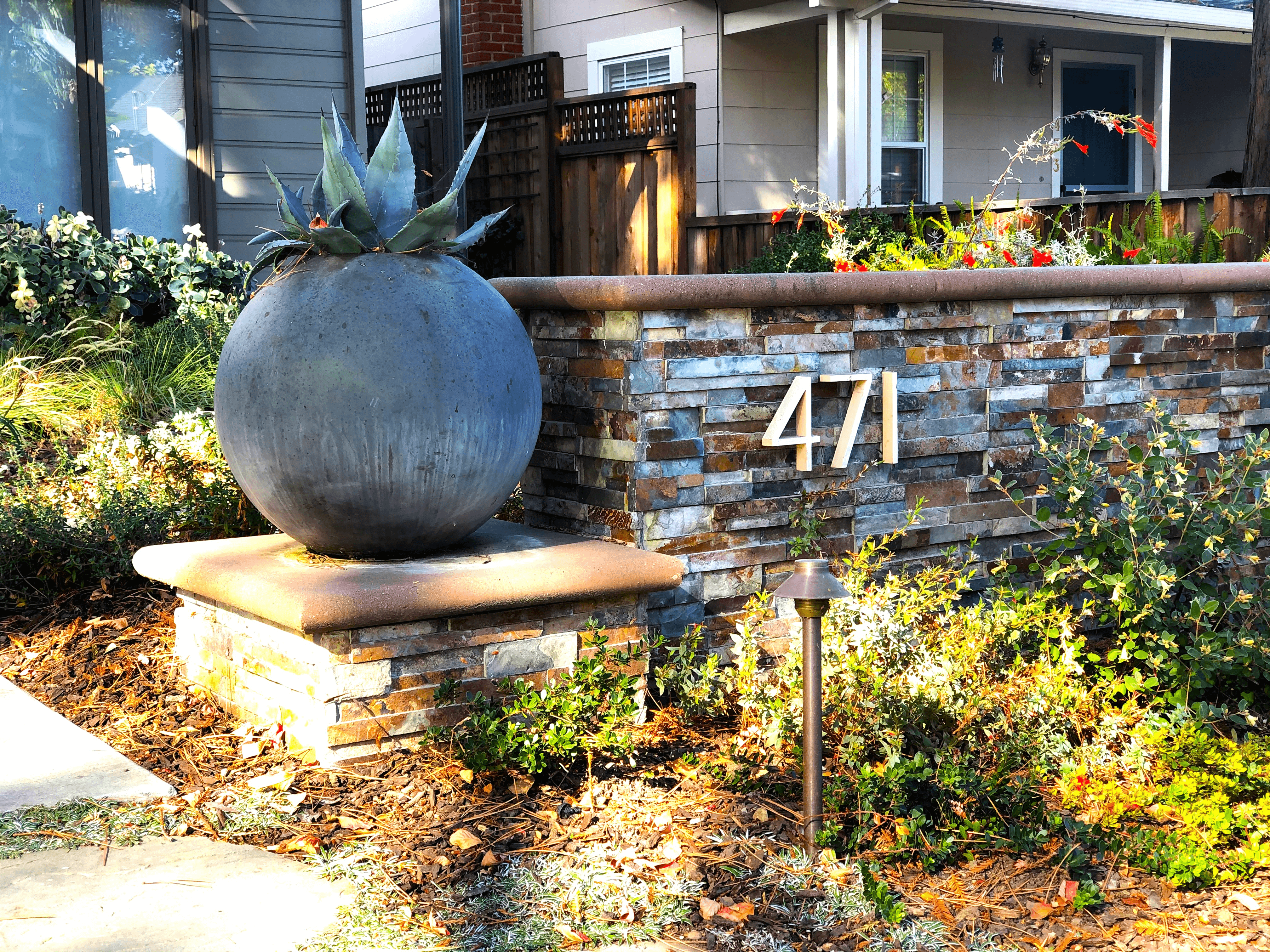 Stacked stone wall at home sidewalk entrance with round planter and large decorative house numbers
