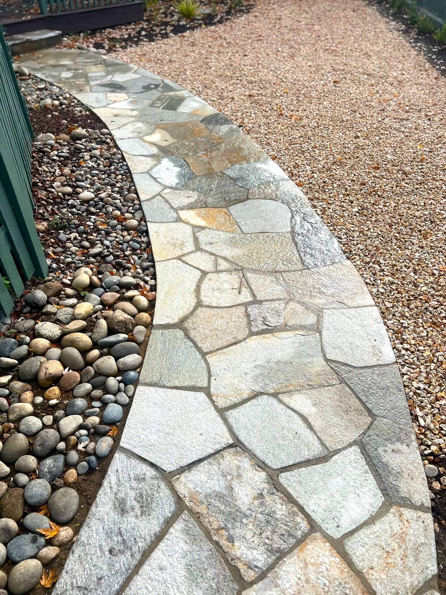 Irregular paver walkway flanked with river roc on one side and grave on the other