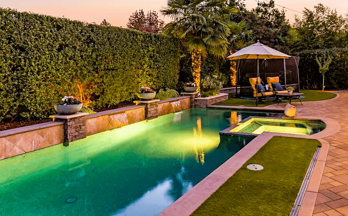 Elegant long rectangular swimming pool with water fall feature in landscaped backyard.