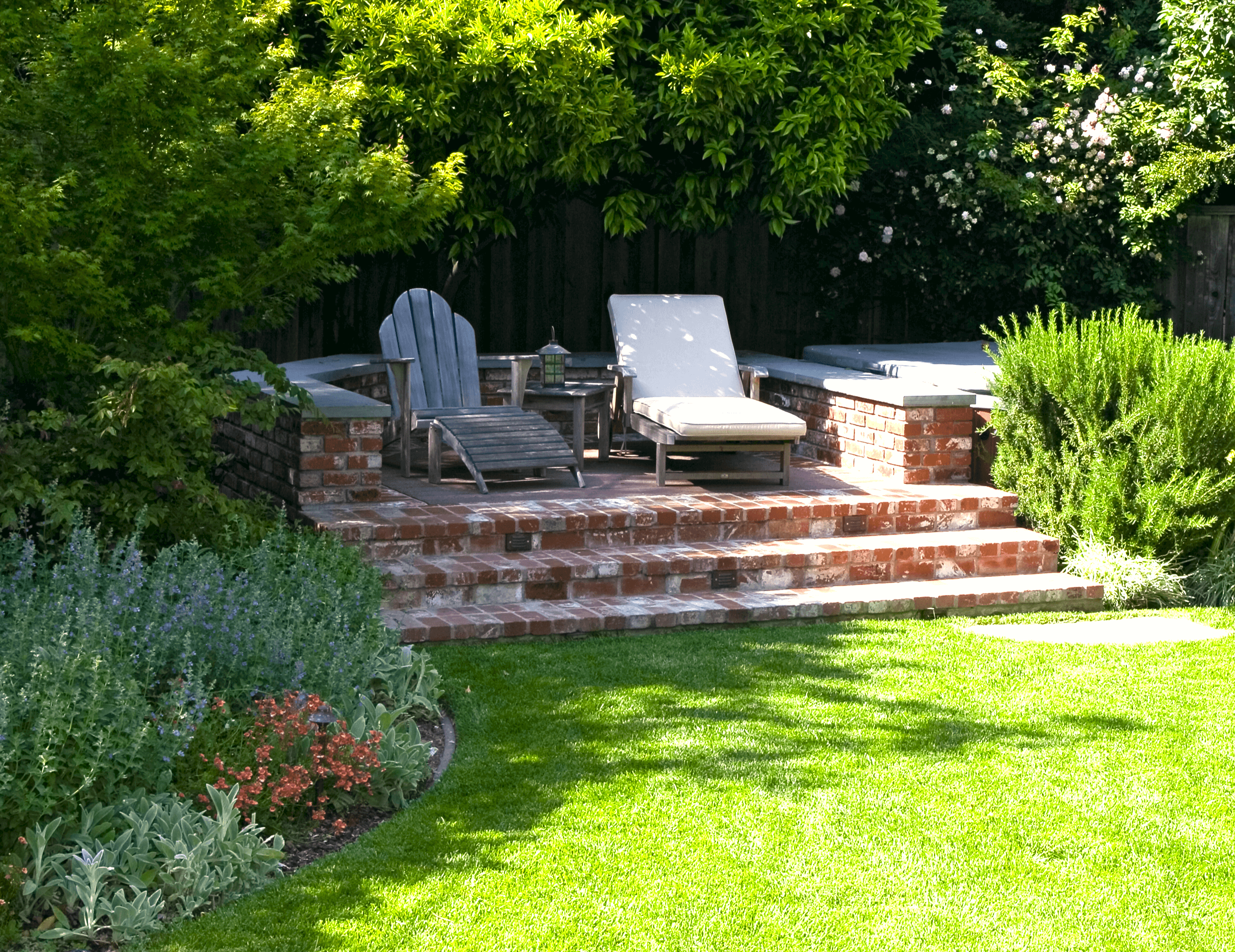 Raised brock patio under trees with lounge chairs and overview of lawn