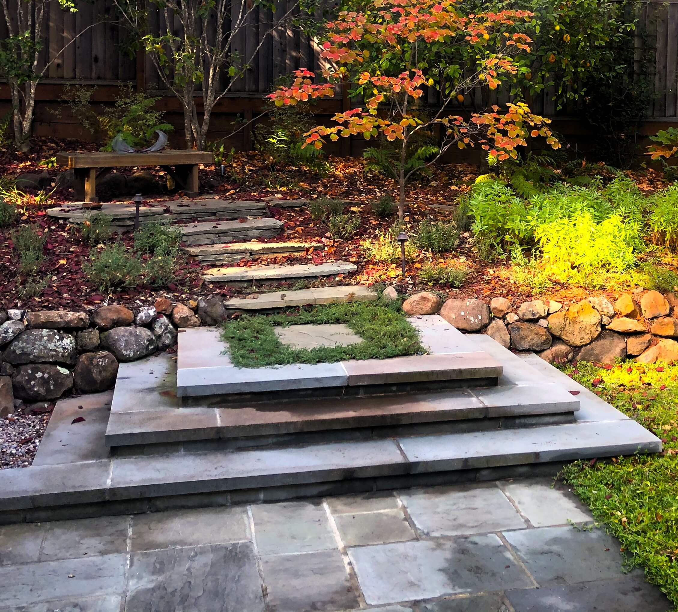 Custom stone steps leading to seating area in backyard amongst trees with fall foliage