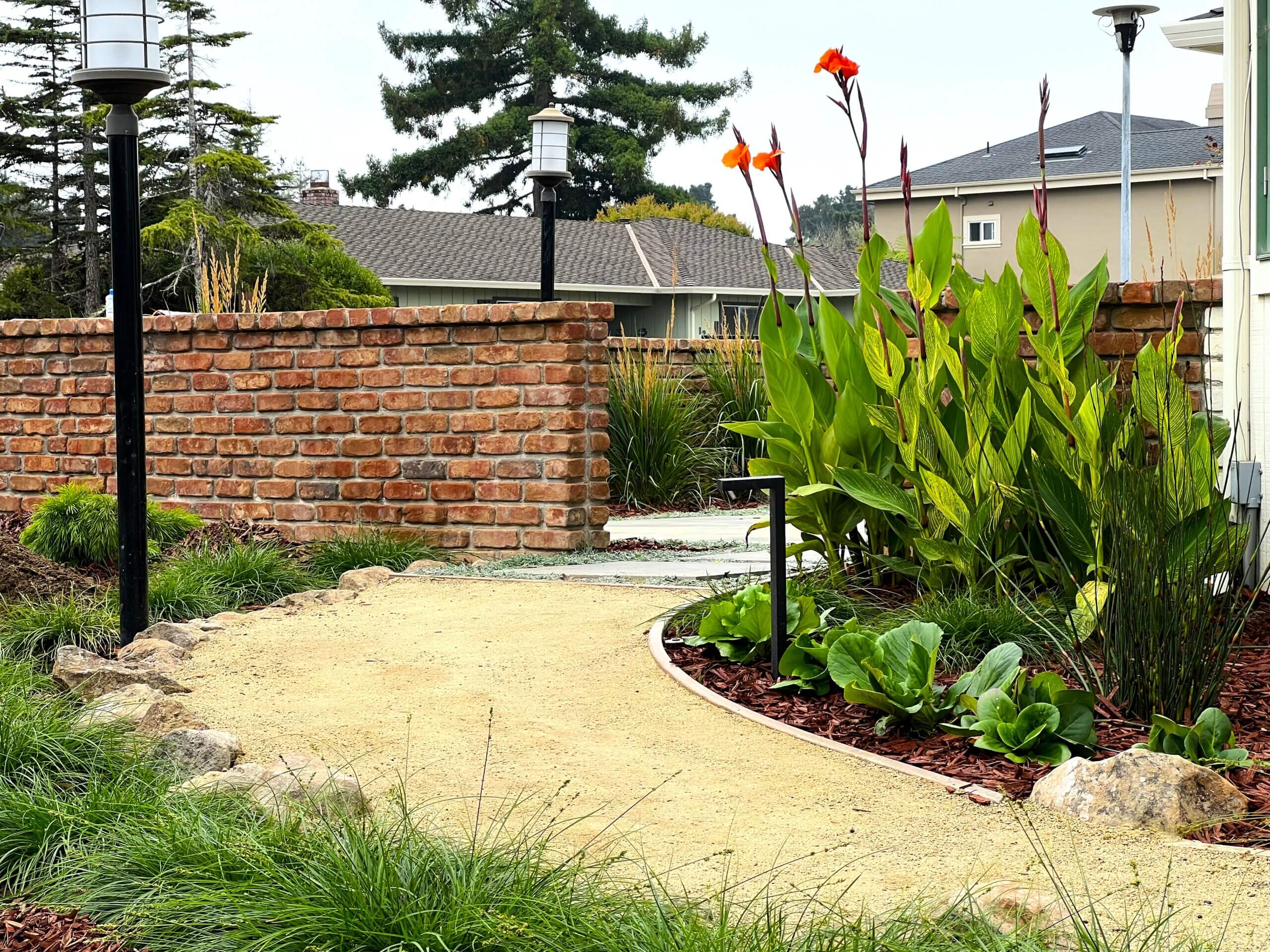 Sand and gravel walkway leading to brick fenced courtyard with ground cover plantings