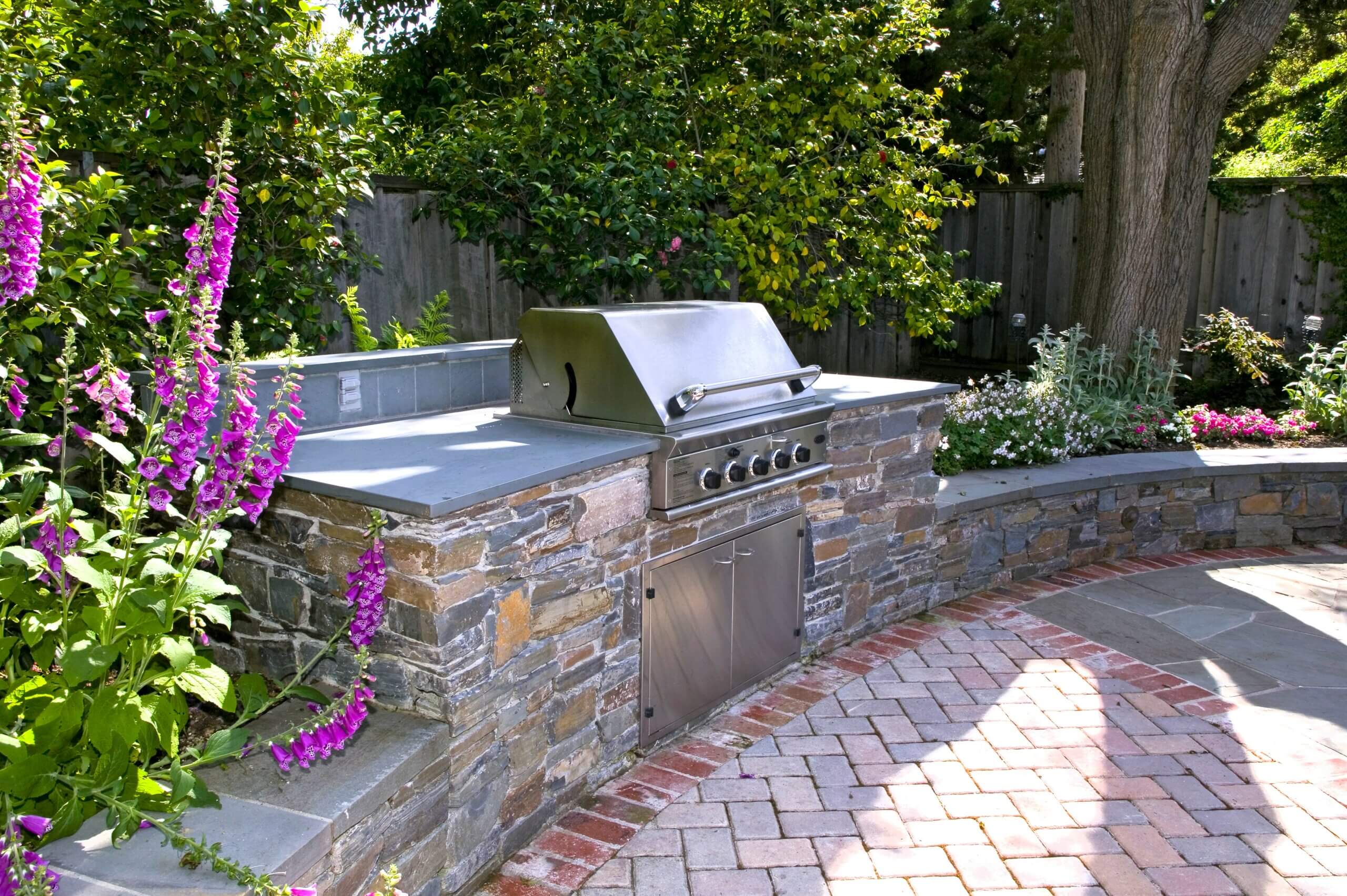 Outdoor kitchen with built-in gas grill, slab counters and stone surround.